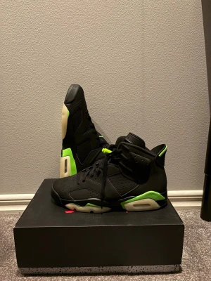 Nike Air Jordan 6 svart/grön sneakers - Nike Air Jordan 6 sneakers i svart med neongröna detaljer och vit sula. Skorna har snörning, hög siluett och perforerade paneler. Jumpman-logga i grönt på tungan och undersidan. Materialet är skinn och syntet, med rund tå och platt sula. Perfekt för dig som gillar streetwear och basketstil.