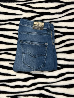 Replay - Säljer ett par snygga blå jeans från Replay med slim fit-passning. Jeansen har klassisk femficksdesign, dragkedja och knapp i midjan samt Replay-logga på linningen. Materialet är mjukt jeans och färgen har coola slitningar för en modern look. W32/L32 Hör av dig vid minsta fundering 😀 