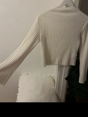 Vit ribbad tröja från Gina Tricot - Säljer en vit ribbad långärmad tröja från Gina Tricot i storlek XS. Tröjan har en croppad passform med långa ärmar och rå kant vid halsen. Perfekt att styla med jeans eller kjol för en clean look.