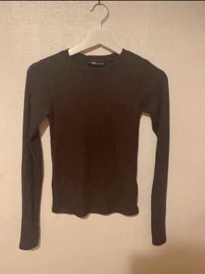 Brun tröja - Säljer en brun långärmad tröja från New Yorker i storlek XS. Tröjan är ribbad och har en rund halsringning. Den är slim fit och sitter snyggt på kroppen, perfekt att styla med jeans eller kjol. Materialet är mjukt och stretchigt, vilket gör den skön att ha på sig.