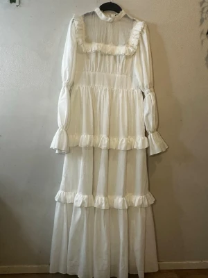 Vit långklänning med volanger - Lång vit klänning från SHEIN i storlek M, med högt hals och långa ärmar. Klänningen har flera lager med volanger och en romantisk look. Materialet är lätt och känns mjukt mot huden. Perfekt för dig som gillar en feminin och drömmig stil.