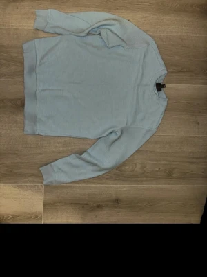 Ljusblå ribbad tröja från H&M - Säljer en ljusblå långärmad tröja från H&M i regular fit. Tröjan har ett ribbat mönster och rund halsringning med breda muddar vid ärmslut och nederkant. Perfekt för dig som gillar enkel och stilren design.