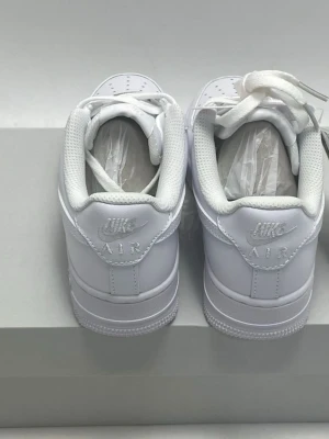 Nike Air Force 1 vita sneakers - Fräscha Nike Air Force 1. Skorna har snörning, rund tå och platt sula. Tillverkade i skinn med perforerade detaljer på ovansidan för extra ventilation. Perfekta för dig som gillar stilrena och tidlösa sneakers. Helt nya oöppnade i låda.