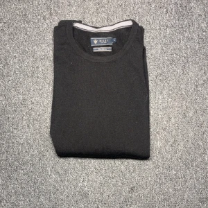 Svart stickad tröja från Riley - En klassisk svart stickad tröja från Riley med rund halsringning och långa ärmar. Perfekt att slänga på sig när det är kyligt ute. Enkel och stilren design som funkar till det mesta.