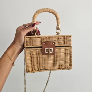 Beige handväska i rotting från Zara - Superfin handväska i beige rotting från Zara med fyrkantig form, brunt skinnspänne och guldfärgade detaljer. Handtaget är lindat och väskan har en kedjerem för axeln. Insidan är fodrad i ljus bomull. Perfekt accessoar för en trendig look.