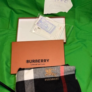  halsduk  Burberry - Snygg halsduk från Burberry med klassiskt rutigt mönster i svart, vitt, grått och rött. Broderad Burberry-logga i guld och fransar i ändarna. Perfekt accessoar för att lyfta din outfit med en lyxig touch.Liknande modell som originalet!