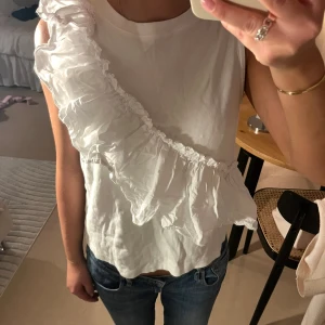 Vit ärmlös topp med volang Part Two - Supersnygg vit ärmlös topp från Part Two med en stor volang som går diagonalt över framsidan. Storlek 36