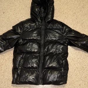 Svart pufferjacka från Manfinity S - Säljer en svart pufferjacka från Manfinity i storlek S. Jackan har glansig finish, huva och dragkedja framtill. Perfekt för kalla dagar med sin vadderade look och klassiska pufferstil. Enkel och stilren design som funkar till det mesta.