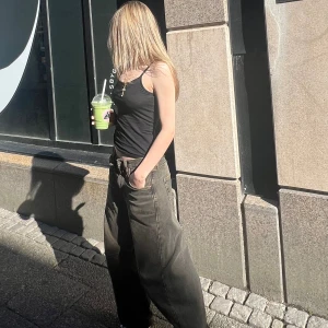 Baggy svarta/bruna jeans från BDG - Säljer ett par svarta baggy jeans från Boohoo med bred passform och låg midja. Jeansen har klassisk femficksdesign, bälteshällor och slitna detaljer för en cool streetstil. Perfekta för dig som gillar oversized och avslappnad look.