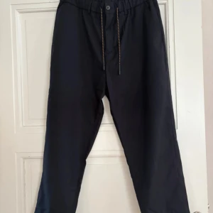 Navy byxor med snörning, strl 48 - Navy/mörkblåa byxor i polyester och viskos med elastisk midja och snörning framtill. Avslappnad passform med raka ben och diskreta bakfickor. Perfekta för en chill och stilren look.