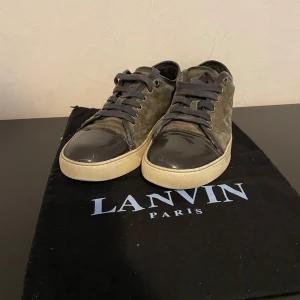 Lanvin skor - Snygga sneakers från Lanvin i mörkgrå mocka med svarta skinn-detaljer på tån och svarta snören. Fint skick 7-8/10. Pris kan diskuteras. Hör av er vid frågor! Storlek 39,5 men passar 40,5. Rekommenderad storlek är 1 större. Dustbag samt box ingår!