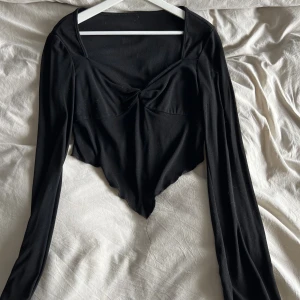 Svart croppad långärmad topp - Säljer en svart långärmad topp med croppad passform. Toppen har en snygg twistad detalj framtill vid bysten och en fyrkantig urringning. Perfekt för dig som gillar trendiga och stilrena plagg.