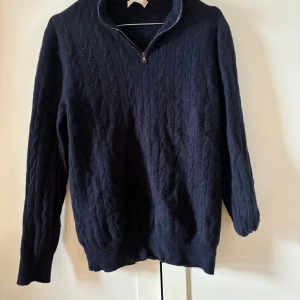 Mörkblå kashmirtröja från Luca Faloni - Säljer en mörkblå kabelstickad tröja från Luca Faloni i lyxig kashmir. Tröjan har half zip-dragkedja vid halsen och långa ärmar. Perfekt för dig som vill ha en stilren och bekväm look med premiumkänsla.