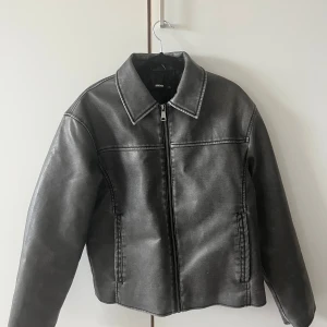 Gråsvart skinnjacka från Bikbok - Snygg skinnjacka från Bikbok med klassisk krage och raka linjer. Jackan har dragkedja framtill och två fickor på sidorna. Perfekt till höst/vinter.  Nypris: 900kr  Mitt pris: 300kr
