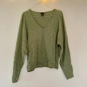 Grön v-ringad blus från Lindex  - Grön blus från Lindex med v-ringning. Blusen har en krinklad struktur och är tillverkad i ett lätt material som känns luftigt och skönt. 