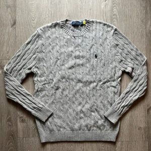 Grå kabelstickad tröja Polo Ralph Lauren - Snygg grå kabelstickad tröja från Polo Ralph Lauren med klassisk rund hals. Perfekt till hösten och vintern. Skön passform och stilren look. Storlek M endast 600kr