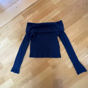 Mörkblå offshoulder topp, Kappahl - Säljer en mörkblå ribbad offshoulder topp från Kappahl i storlek 158/164. Toppen har långa ärmar och en bred, vikt kant över axlarna för en snygg och trendig look. Perfekt att styla med jeans eller kjol för en cool outfit. Perfekt till höst/vintern