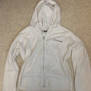 Vit kofta från Project Sport - Vit kofta från Project Sport med dragkedja framtill. 'Active Sport'-logga på bröstet. Tröjan har huva med snörning och två fickor framtill. Tillverkad i mjuk frotté. Storlek L men passar även storlek M