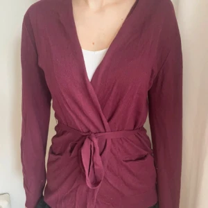 Vinröd omlottkofta med knytband - Säljer en vinröd omlottkofta med knytband i midjan och långa ärmar. Ganska tunt material. 