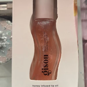 Gisou honey infused lip oil - Säljer en Gisou honey infused lip oil i en snygg vågig flaska. Färgen är glansig och persikotonad med små skimrande glitterpartiklar. Perfekt för att ge läpparna en juicy och återfuktad look. Kommer i originalförpackning. Den är helt ny och originalpriset är 349💕pris kan diskuteras