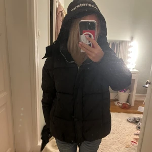 Svart pufferjacka från Svea - Säljer en svart pufferjacka från Svea med stor huva och logga på huvan. Jackan har dragkedja framtill och är riktigt varm och skön för kalla dagar. Har litet hål vid blixtlåsen