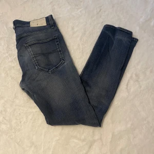 Blå jeans från Tiger of Sweden 30/32 - Snygga blå jeans från Tiger of Sweden med klassisk femficksdesign och diskreta slitningar. Jeansen har normal passform och raka ben, tillverkade i mjukt denimtyg. Perfekta för en stilren och avslappnad look.