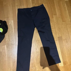 Svarta chinos med rak passform - Snygga svarta chinos med klassisk rak passform och diskreta fickor. Byxorna har bälteshällor och stängs med knapp och dragkedja. Perfekta för en clean och stilren look. Materialet känns mjukt och följsamt, vilket gör dem bekväma hela dagen.Storleken 170/82 på byxor ungefär 170 cm lång och har ett midjemått på 82 cm.