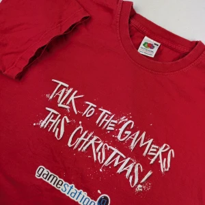 Retro 2011 Christmas Gamestation t-shirt Size M from Fruit of the Loom - Röd t-shirt från Fruit of the Loom med trycket 'Talk to the gamers this Christmas!' och gamestation-logga på framsidan. Baksidan har texten 'STAFF GAMER' i vitt. Klassisk passform och rund hals, tillverkad i mjuk bomull. 100% cotton  Retro/vintage from 2011  Armpit to armpit approx 50cm  Length approx 65cm