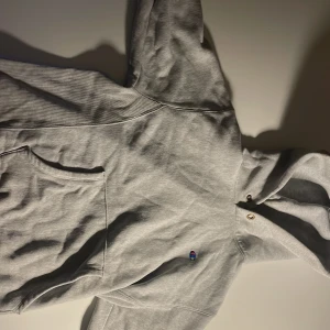 Grå hoodie från Champion M - Säljer en grå hoodie från Champion i storlek medium. Klassisk modell med huva, magficka och broderad Champion-logga på bröstet och ärmen. Tillverkad i mjuk bomullsmix, perfekt för chill eller skola.