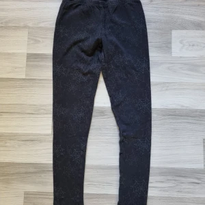 Svarta leggings med spindelnätsmönster Ellos - Svarta leggings från Ellos med coolt spindelnätsmönster över hela byxan. Mjukt och stretchigt material som sitter skönt och följer kroppen. Perfekta för dig som vill sticka ut med en unik och edgy stil.