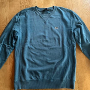 Blå sweatshirt från Lee - Säljer en stilren blå sweatshirt från Lee med broderad logga på bröstet. Tröjan har rund halsringning, ribbade muddar och är långärmad. Perfekt för dig som gillar enkel och clean stil.
