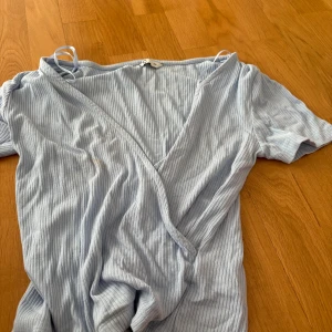 Ljusblå ribbad omlottröja XS - Supersöt ljusblå tröja från C i storlek XS. Klänningen har ribbat tyg, omlott-skärning och korta ärmar. Perfekt för dig som gillar en enkel men ändå stilren look. Säljes då den inte längre kommer till användning.