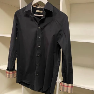 Svart Burberry skjorta med rutiga detaljer - Säljer min killes Burberry skjorta pågrund av att den har blivit för liten för honom. Skjortan är i väldigt bra skick och noggrant omhändertagen Kom privat för intresse eller frågor🤍🤗