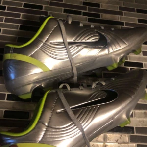 R9 fotbollsskor  - Skick 9/10 nypris 5-6 tusen. Säljer ett par riktigt snygga Nike fotbollsskor i metallic silver med svarta swoosh-loggor och limegröna detaljer. Skorna har snörning, mönstrad yttersula och är tillverkade i syntetmaterial. Perfekta för dig som vill sticka ut på planen.