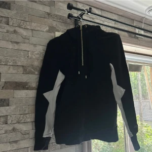 Svart och vit hoodie från Elly Pistol - Säljer en svart hoodie från Elly Pistol i storlek S. Tröjan har vita detaljer längs ärmarna och stor vit logga på ryggen. Utrustad med huva, snörning och en snygg guldig half zip-dragkedja framtill. Perfekt för dig som gillar streetstyle och vill sticka ut.