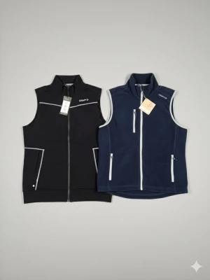 Paketpris. Svart och marinblå Craft väst - Två sportiga västar från Craft i storlek M. En svart väst i syntetmaterial med vita detaljer och dragkedja framtill samt fickor. Den andra är marinblå i fleece med ljusa dragkedjor och tre fickor. Perfekta för lager-på-lager och outdoor.