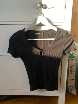 Svart ribbad topp från Bik Bok - Säljer en svart ribbad topp från Bik Bok i storlek XS. Toppen har korta ärmar, v-ringning med en liten knutdetalj framtill och är gjord i mjuk bomullsmix. Perfekt för att styla med jeans eller kjol.