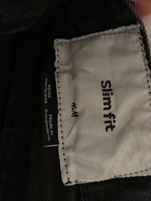 Svarta slim fit jeans från H&M - Svarta slim fit jeans från H&M med klassisk femficksdesign och smal passform. Jeansen har normal midja och är tillverkade i ett mjukt bomullsmaterial med lite stretch för extra komfort. Perfekta för dig som gillar en stilren och enkel look.