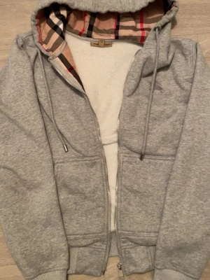 Burbbery Zip - Mycket fin och unik Burbbery zip i gråa färgen, tröjan kommer i helt nytt skick med alla orginal taggar och tillbehör. Tröjan är jätte värmandes till vintern och är i storlek S. Men sitter inte liten !!!