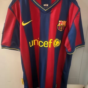 Fcb Barcelona t-shirt - Bilderna visar en FC Barcelona fotbollströja från Nike med rödblåa ränder, klubbmärke, LFP-patch och Unicef-logga. 