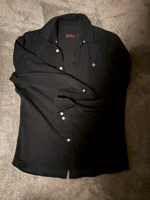 Svart skjorta från Morris - Snygg svart skjorta från Morris med klassisk krage och vita knappar. Skjortan är gjord av bomull, jag säljer den för att den blivit lite för kort. Hör av er vid minsta funderingar!!