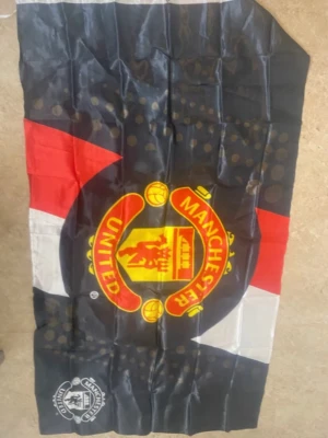 Manchester United väst i polyester - Säljer en svart, röd och vit väst med Manchester Uniteds ikoniska klubbmärke tryckt på framsidan. Västen har en sportig look och är tillverkad i glansig polyester, perfekt för dig som vill visa ditt stöd för laget. Passar dig som gillar fotboll och vill sticka ut.