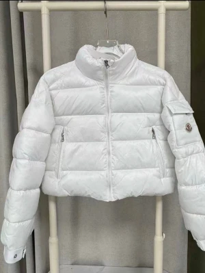 Vit pufferjacka från Moncler - Säljer en riktigt snygg vit pufferjacka från Moncler. Jackan har hög krage, dragkedja framtill, två sidofickor med dragkedja och en ficka med Moncler-logga på ärmen. Croppad modell med quiltad design och långa ärmar.