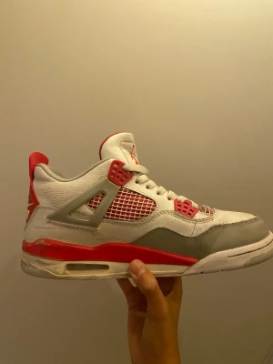 Nike SB Air Jordan 4 vit/röd sneaker - Nike SB Air Jordan 4 sneakers i vitt, rött och grått. Skorna har meshpaneler, klassisk snörning och tydliga röda detaljer på häl och sula. Ovandelen är i skinn och mesh, med Nike SB-logga bak. Perfekt för dig som gillar streetwear och ikoniska modeller.
