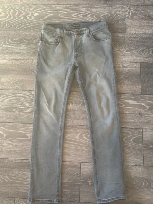  Nudie Jeans - Säljer ett par gråa skinny jeans från Nudie Jeans i storlek W32 L30. Jeansen har klassisk femficksdesign, svarta sömmar och Nudie-logga på bakfickan. Materialet är stretchigt jeans och passformen är tight med smal siluett.