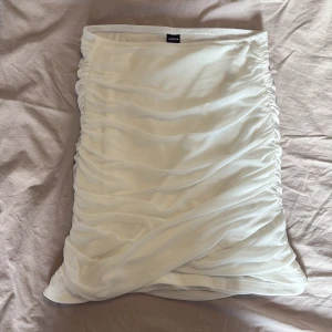 Vit omlottkjol från SHEIN - Supersnygg vit kortkjol från SHEIN i omlottmodell med draperade detaljer längs sidorna. Kjolen har en tight passform och är gjord i ett tunt, syntetiskt material som ger en fräsch och clean look. Perfekt att styla med crop top eller oversized hoodie.