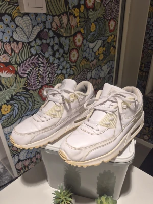 Nike Air Max 90 vita sneakers EUR44 passar 43 - Fräscha Nike Air Max 90 sneakers i helvitt med krämfärgade detaljer. Klassisk chunky siluett med synlig Air-enhet i sulan, snörning och rund tå. Ovandel i skinn och syntet, insida i mjukt tyg. Perfekta för dig som gillar stilrena och sportiga sneakers.