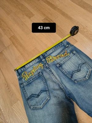 Replay Brand blå jeans med broderi - Säljer ett par Replay Brand jeans i blå tvättad denim med coolt broderi i gult och rött över bakfickorna. Klassisk femficksmodell med raka ben och slitningar framtill. och de har en normal passform. Perfekt för dig som gillar streetwear och detaljer.