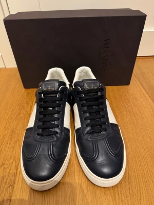 Mörkblå Valentino Flycrews  - Säljer ett par trendiga sneakers från Valentino Garavani i mörkblått och vitt skinn. Väldigt eftertraktade och exklusiva skor då de inte tillverkas längre. Använda ett fåtal gånger och är i väldigt bra skick då alla nitar också sitter kvar. Mitt pris: 3599, men pris kan diskuteras vid snabb affär. Skriv vid minsta fundering eller fråga!