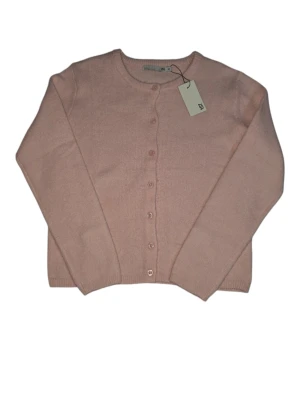 Ljusrosa kofta från 157 - Supersöt ljusrosa kofta från 157 med rund hals och knappar framtill. Koftan är stickad och har långa ärmar samt ribbade muddar vid hals, ärmslut och nederkant. Perfekt att slänga på sig när det är lite kyligt ute.